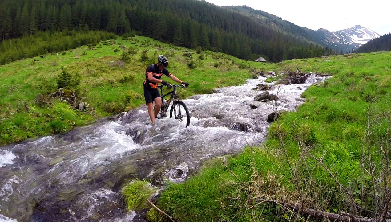 biker pushing his bike through a mountain stream