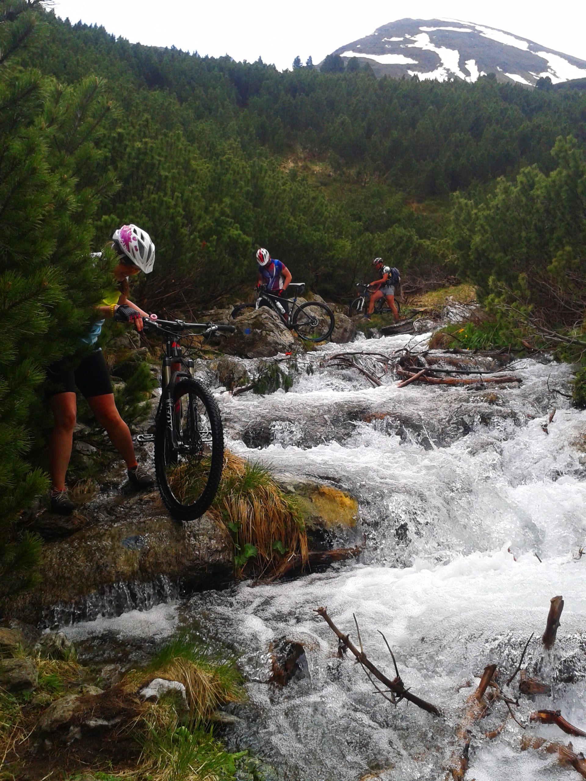 three mountain bikers pushing bikes next to a mountain stream
